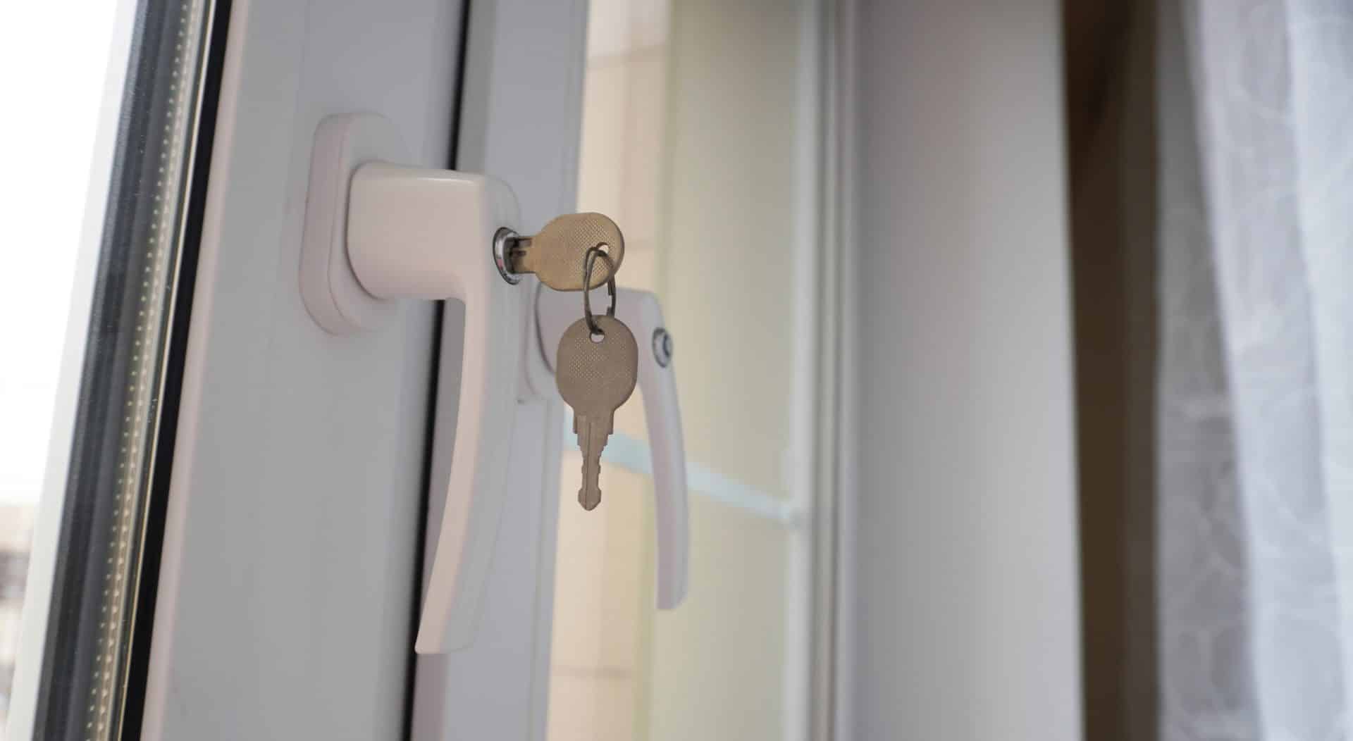 window-lock-2 Close-Up of Locked White PVC Window Handle with Two Inserted Keys in Bright Interior with Sheer Curtain, Representing Home Safety, Modern Security, and Window Lock Mechanism Concept